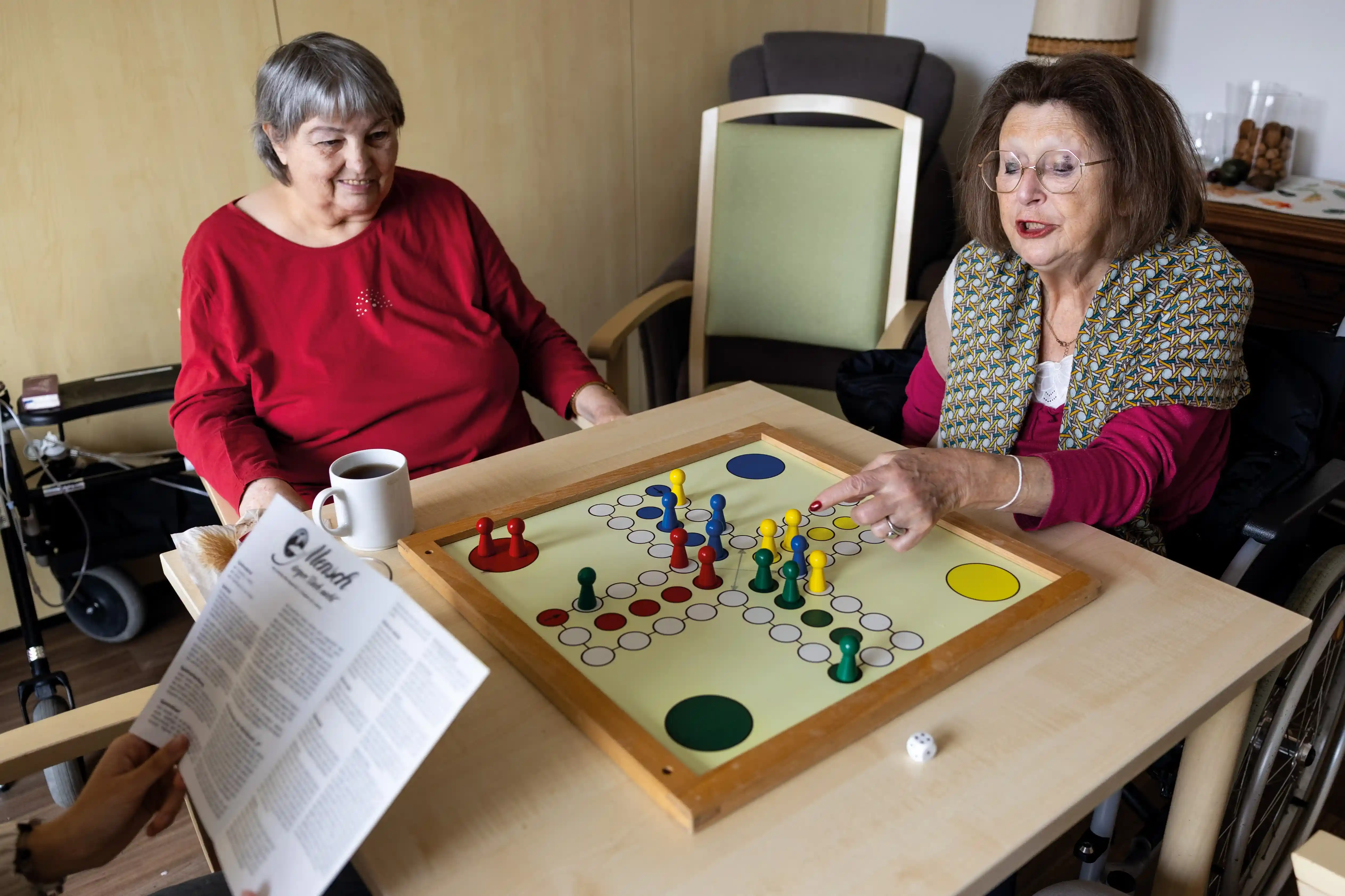 Zwei Seniorinnen spielen gemeinsam Mensch ärgere dich nicht in einem Pflegeheim.